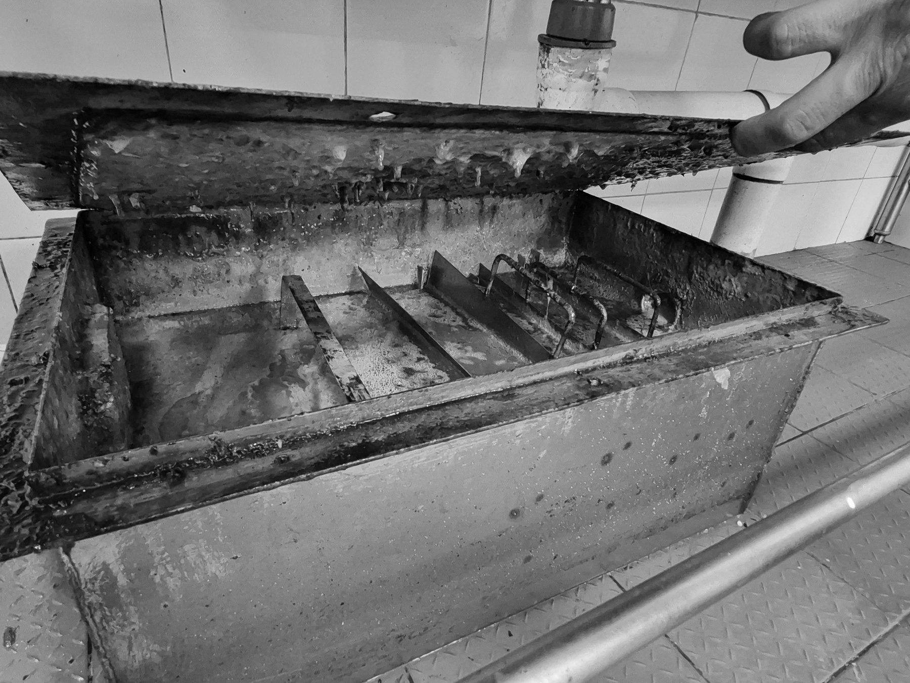 Trampa de grasa abierta en la cocina de un establecimiento, con acumulación visible en sus cámaras.